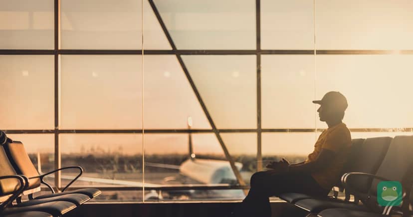 A traveler waits alone at an airport gate beside a window